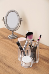 Organizer with cosmetic products for makeup and mirror on table against light wall