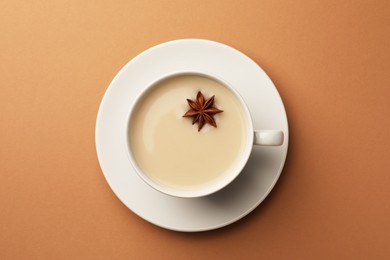 Cup of tea with milk and anise star on brown background, top view