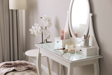 Wooden dressing table with decorative elements and makeup products in room. Interior design