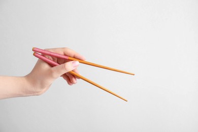 Photo of Woman holding pair of wooden chopsticks on light grey background, closeup