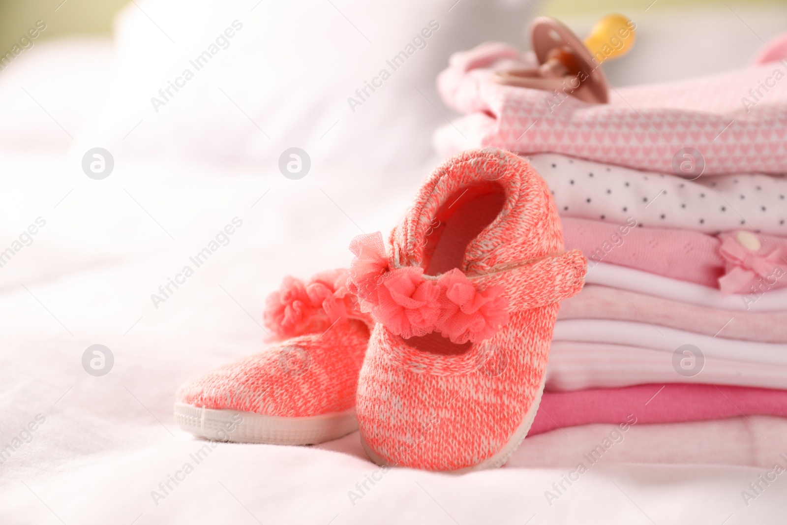 Photo of Stack of baby girl's clothes, pacifier and shoes on bed, closeup. Space for text