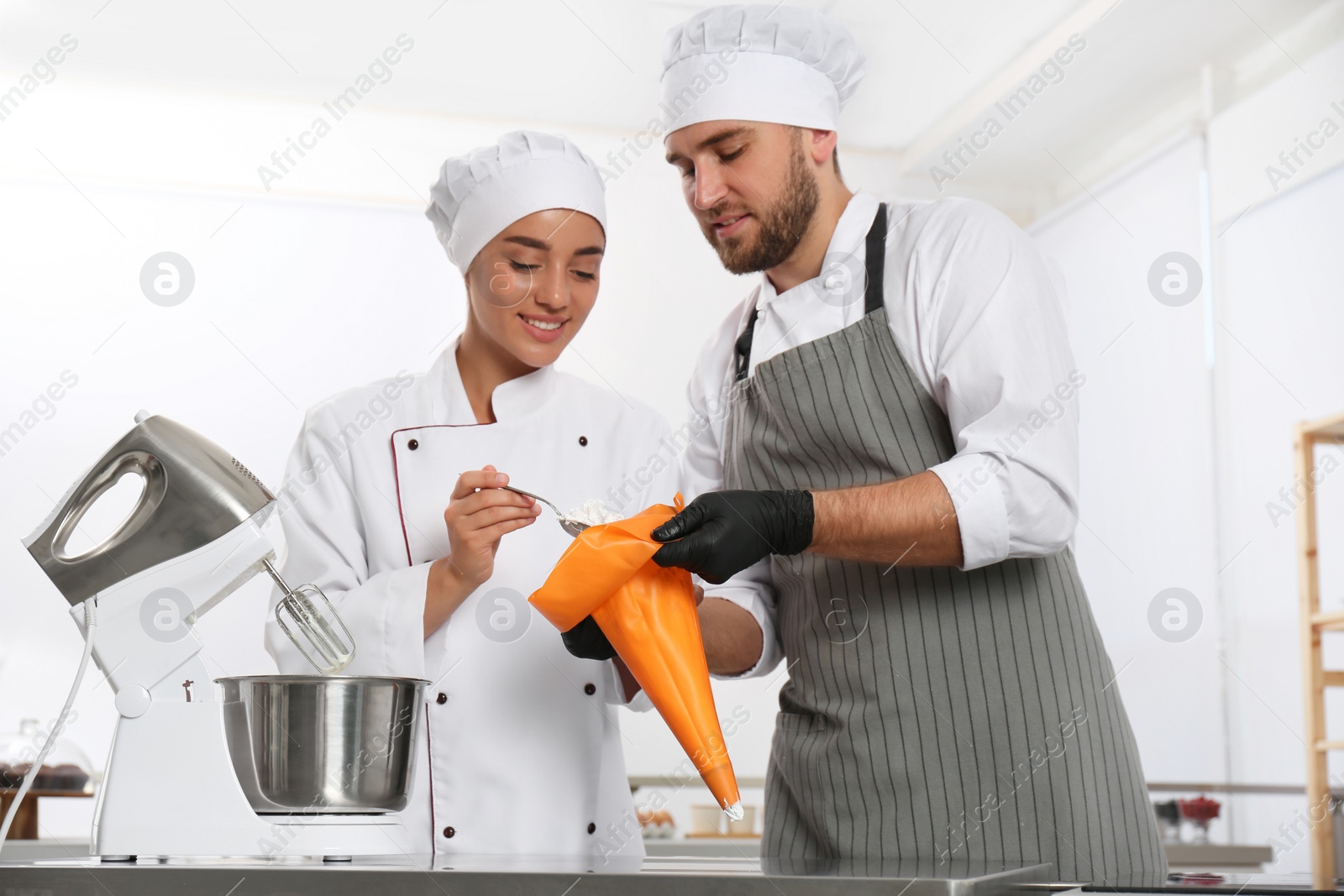 Photo of Pastry chefs preparing cream at table in kitchen