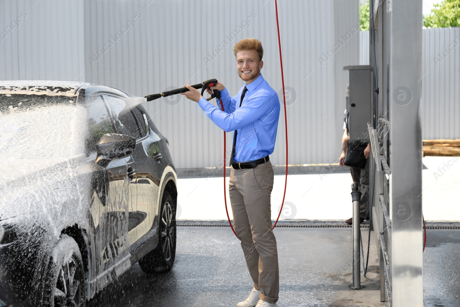 Photo of Businessman cleaning auto with high pressure water jet at self-service car wash