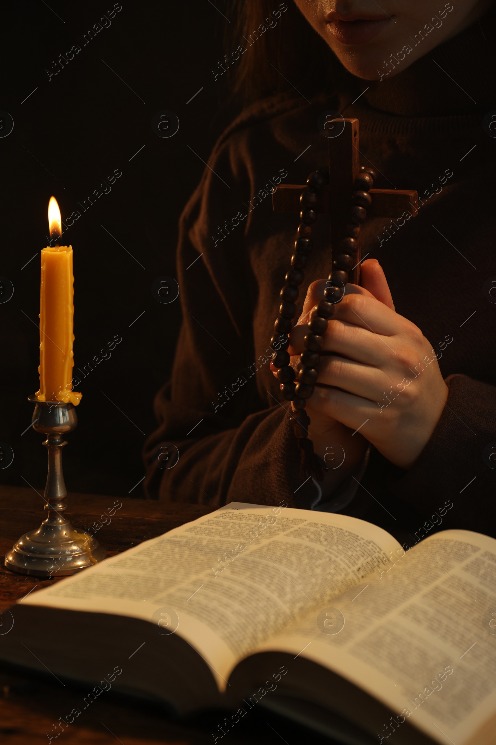 Photo of Woman praying at table with burning candle and Bible, closeup