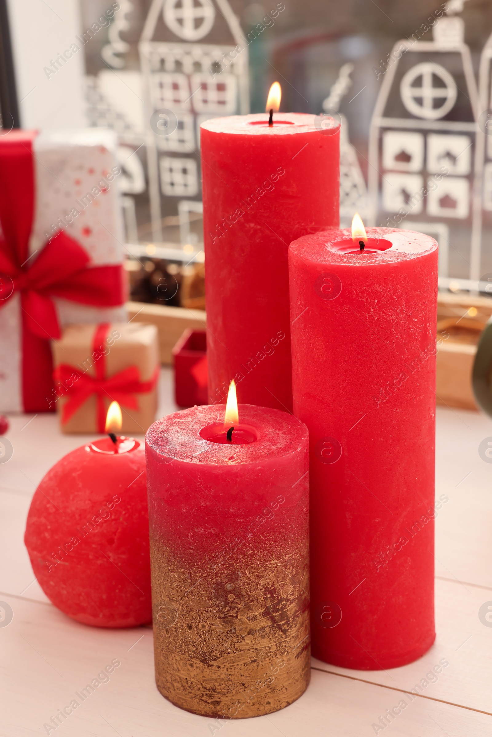 Photo of Beautiful burning candles with Christmas decor on white wooden table near window