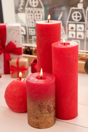 Beautiful burning candles with Christmas decor on white wooden table near window