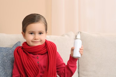Photo of Cute little girl holding nasal spray on sofa indoors