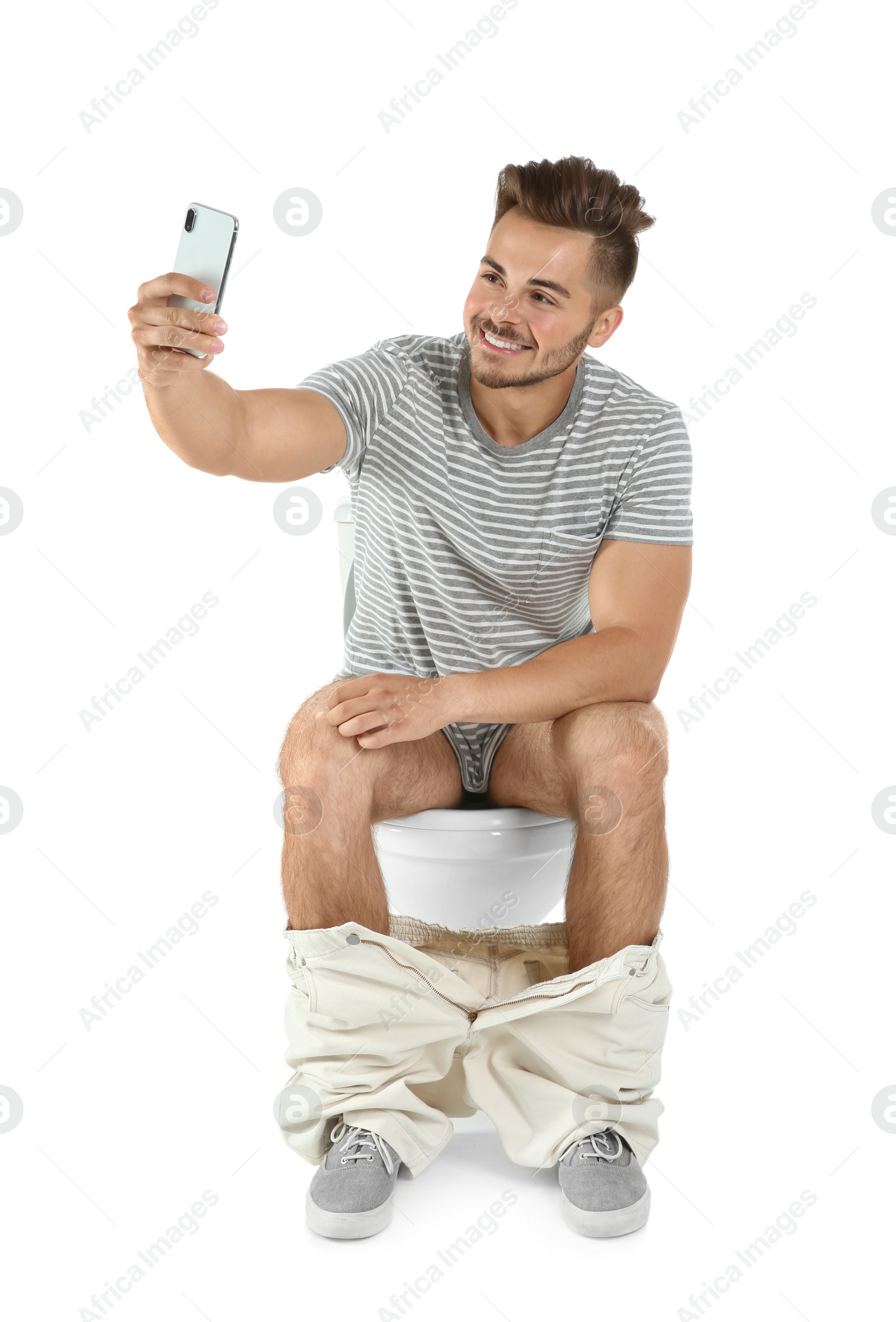 Photo of Young man taking selfie while sitting on toilet bowl. Isolated on white