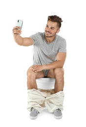 Young man taking selfie while sitting on toilet bowl. Isolated on white