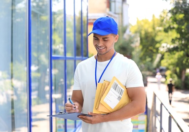 Photo of Young courier with padded envelopes and clipboard outdoors. Delivery service