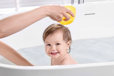 Mother bathing her cute little baby in tub at home