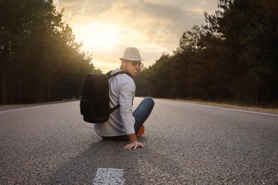 Photo of Man with backpack sitting on road near forest