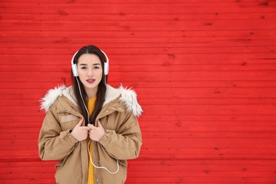 Beautiful young woman listening to music with headphones against color wall. Space for text