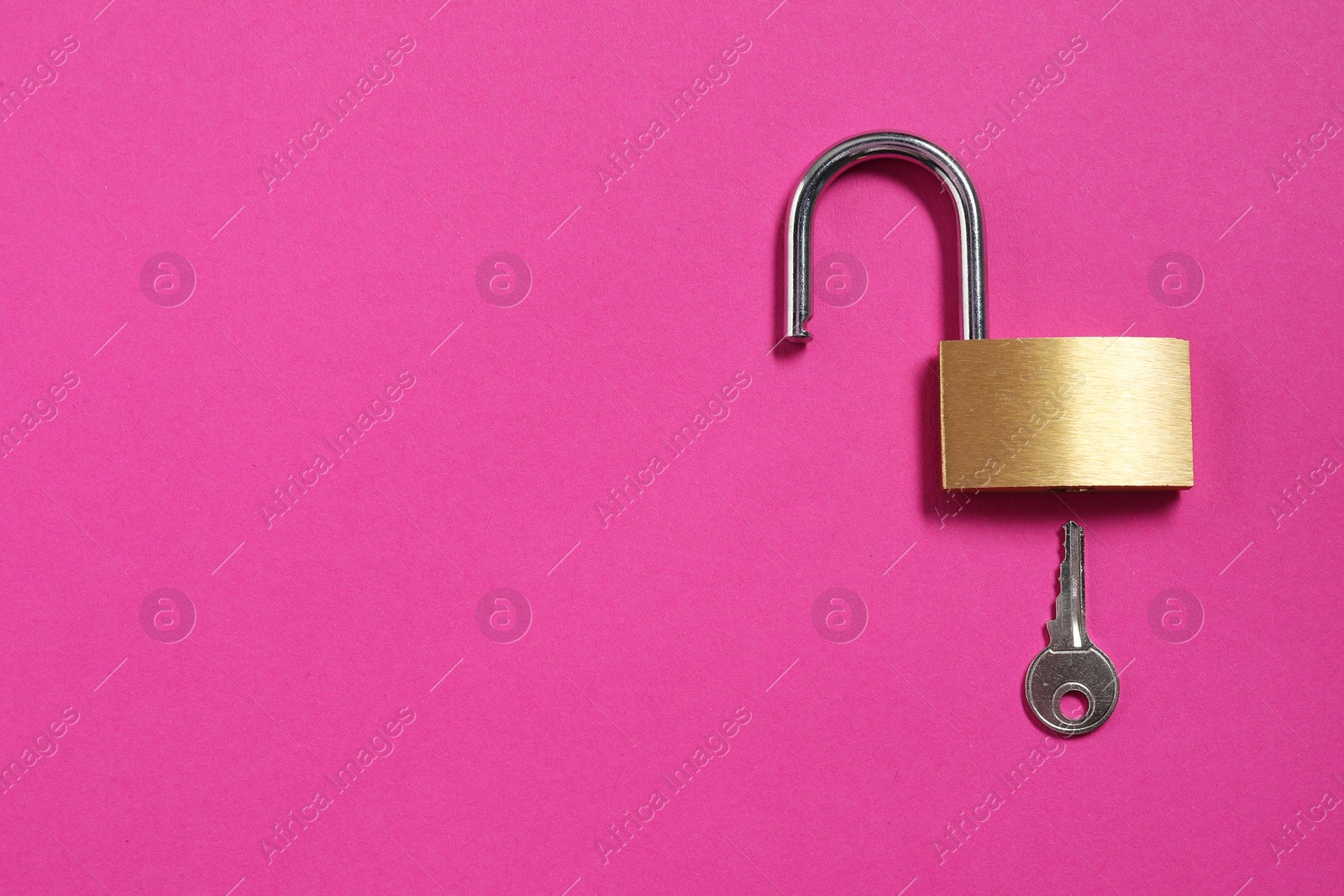 Photo of Steel padlock with key on pink background, top view. Space for text