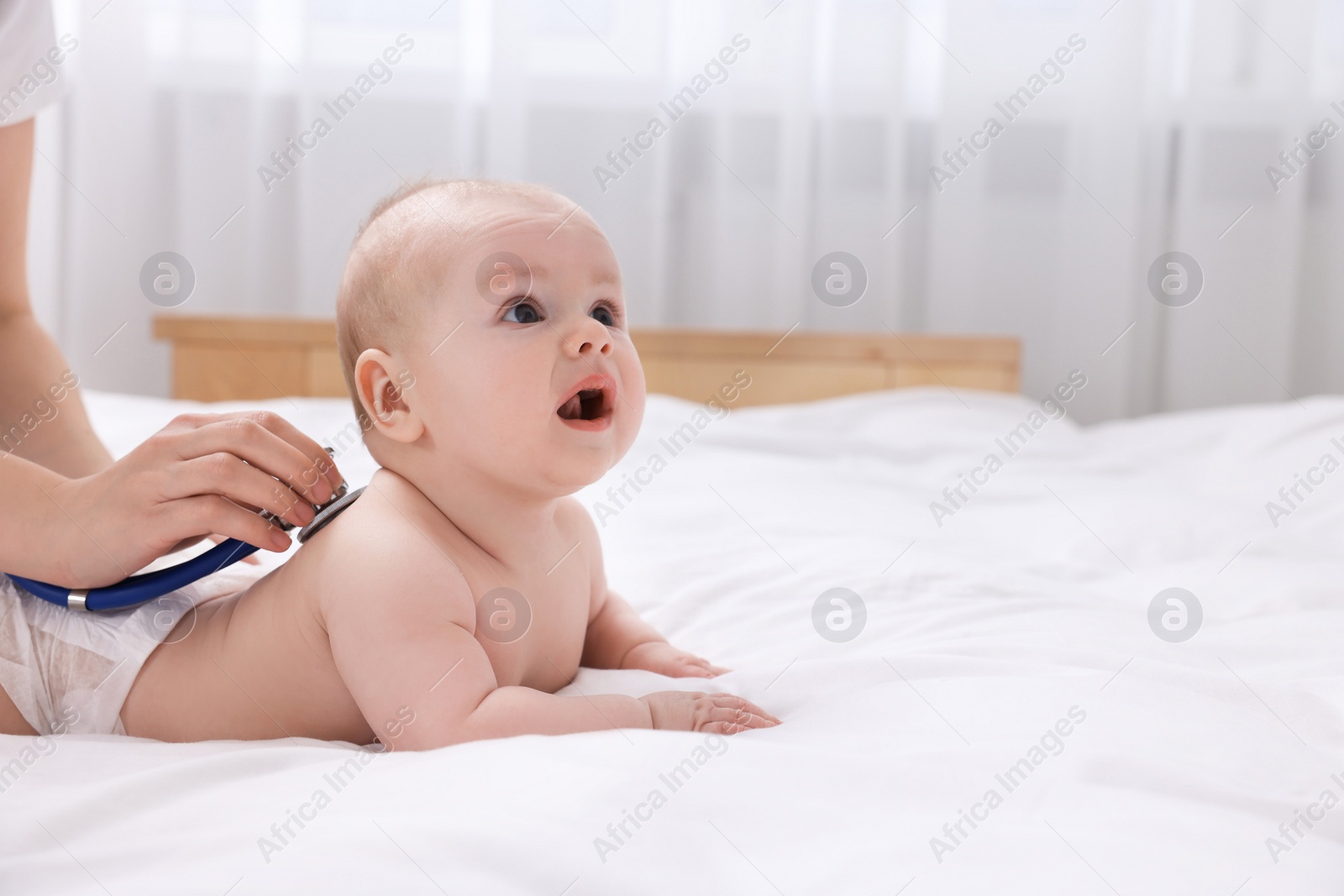 Photo of Pediatrician examining cute little baby with stethoscope in clinic, closeup. Space for text