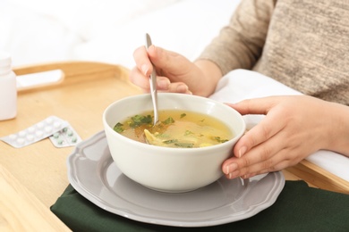 Photo of Sick young woman eating broth to cure cold in bed, closeup