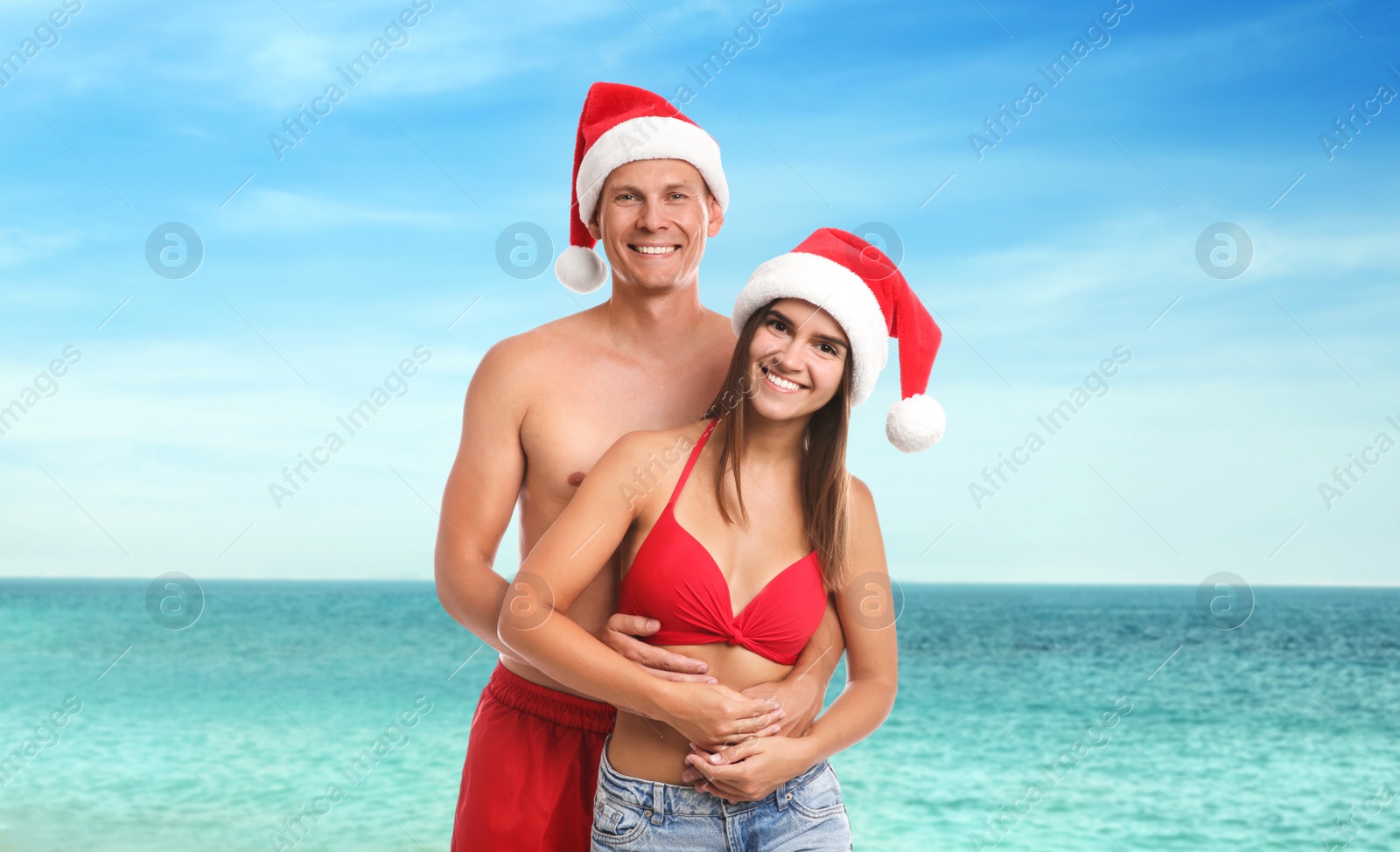 Image of Happy couple wearing Santa hats near sea. Christmas vacation