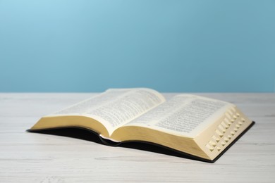 Photo of Open Bible on white wooden table against turquoise background. Christian religious book