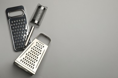 Photo of Different modern graters on grey background, flat lay. Space for text