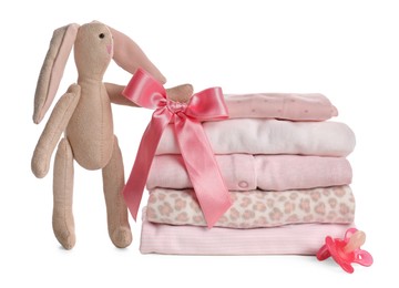 Stack of baby girl's clothes, pacifier and toy bunny on white background