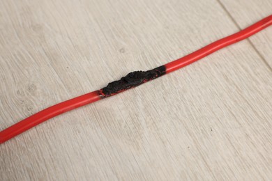 Burnt red wire on wooden floor, closeup. Electrical short circuit