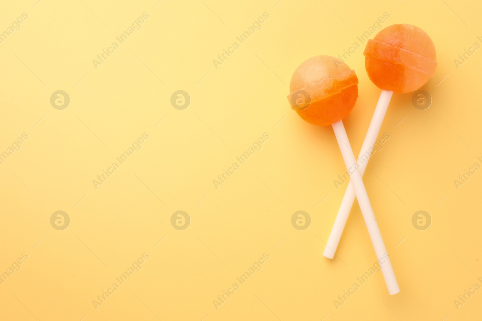 Photo of Tasty lollipops on yellow background, flat lay. Space for text