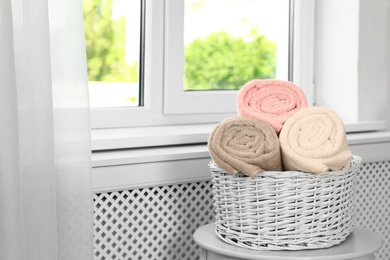 Photo of Basket with clean soft towels on table near window. Space for text