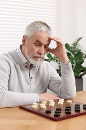 Photo of Playing checkers. Concentrated senior man thinking about next move at table in room