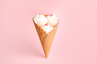 Photo of Delicious vanilla ice cream in wafer cone on pink background