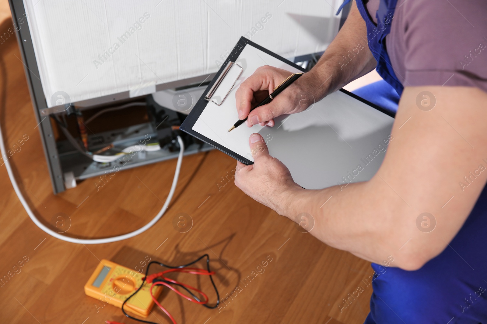 Photo of Male technician examining broken refrigerator indoors, closeup