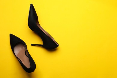 Photo of Pair of elegant black high heel shoes on yellow background, flat lay. Space for text