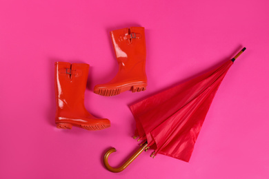 Photo of Beautiful red umbrella and rubber boots on pink background, flat lay