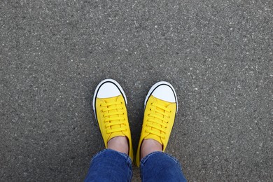 Photo of Woman in stylish gumshoes on asphalt, top view