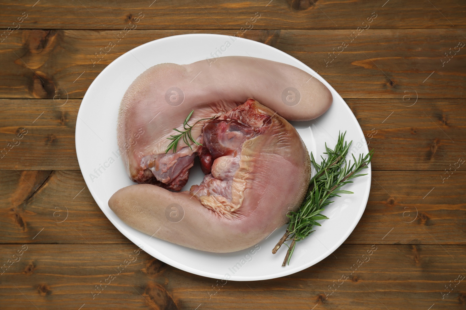 Photo of Plate with raw beef tongues and rosemary on wooden table, top view