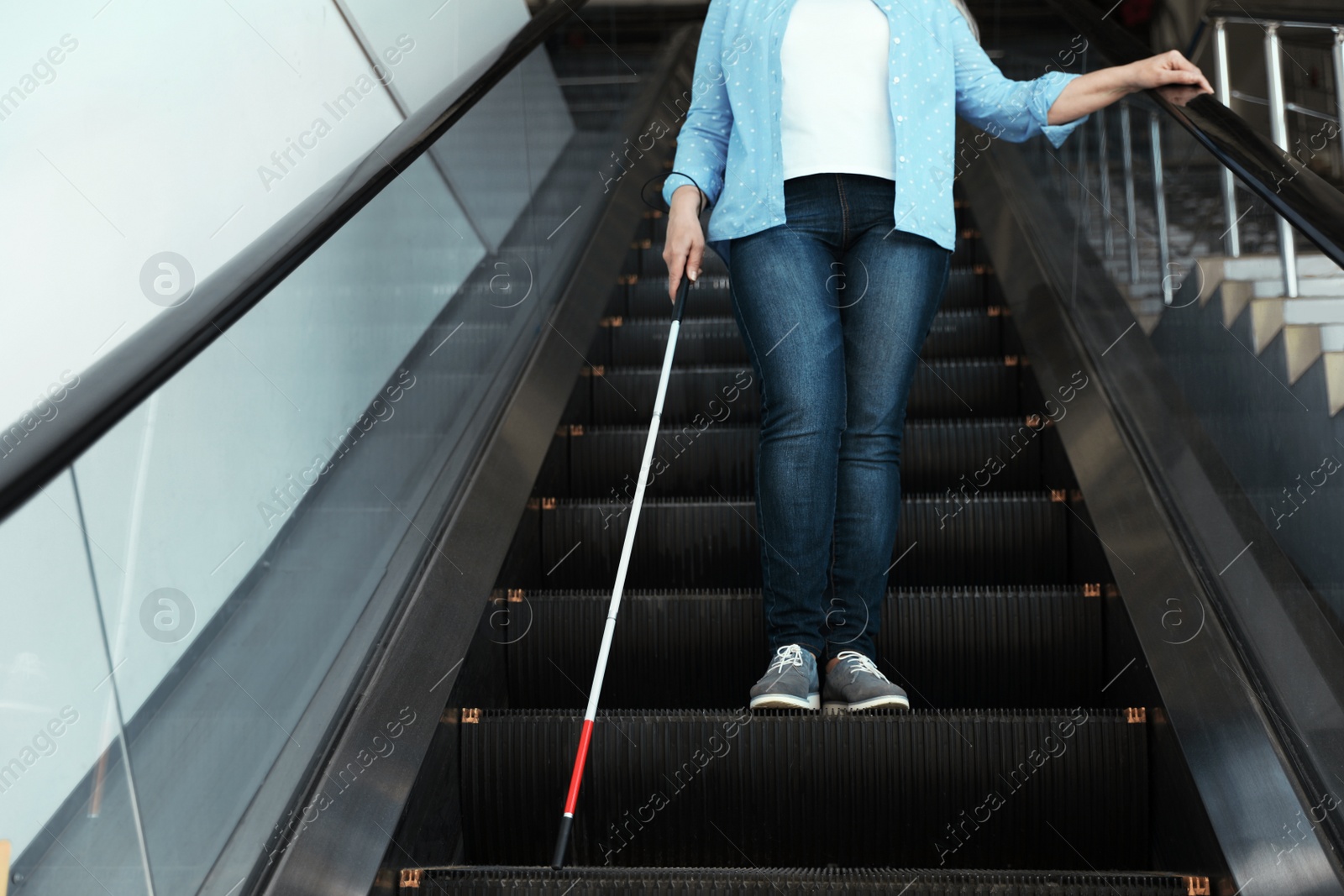 Photo of Blind person with long cane on escalator indoors