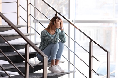 Photo of Emotional teenage girl sitting on stairs indoors