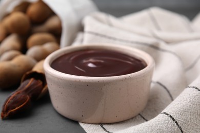 Photo of Bowl of tamarind sauce and fresh pods on table, closeup