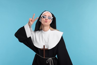 Woman in nun habit showing peace sign against light blue background