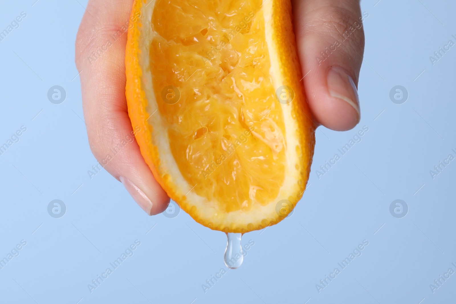 Photo of Woman squeezing juicy orange on light blue background, closeup