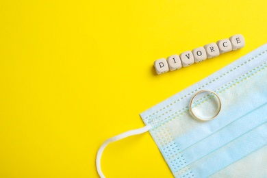Photo of Flat lay composition with protective mask and wedding ring on yellow background, space for text. Divorce during coronavirus quarantine
