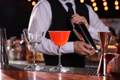 Bartender preparing fresh alcoholic cocktail and martini glass on bar counter, closeup