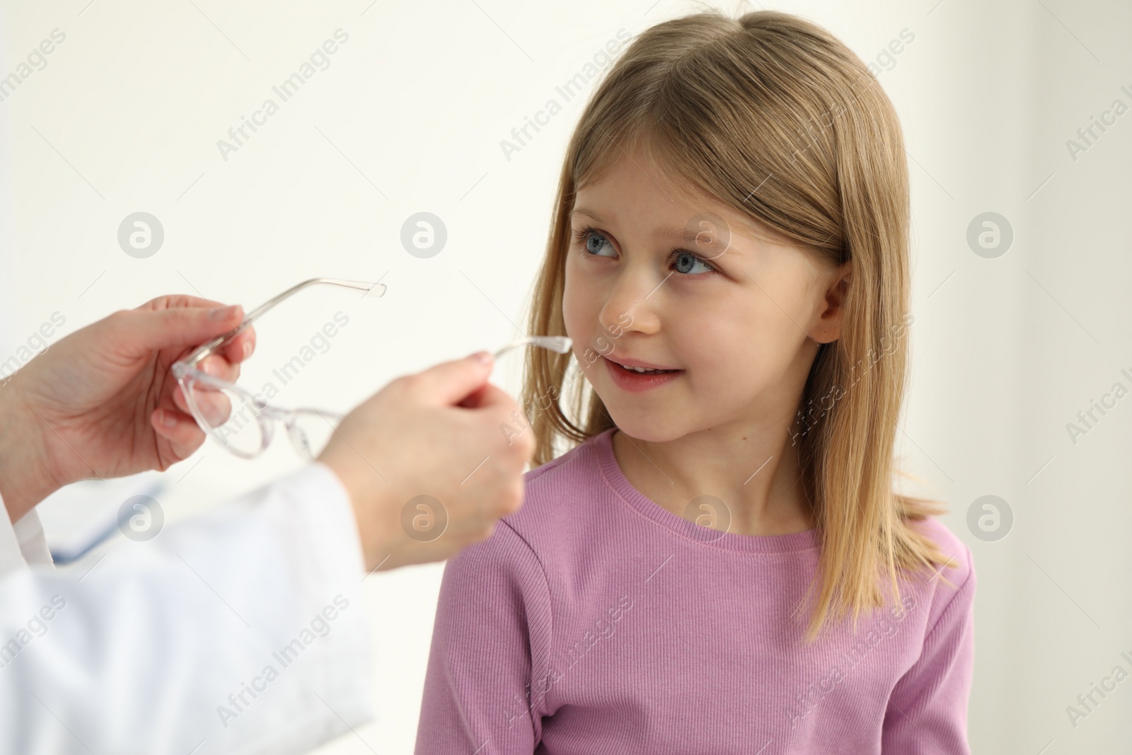 Photo of Vision testing. Ophthalmologist giving glasses to little girl indoors