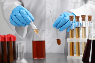 Photo of Scientist dripping brown liquid from pipette into beaker at table, closeup