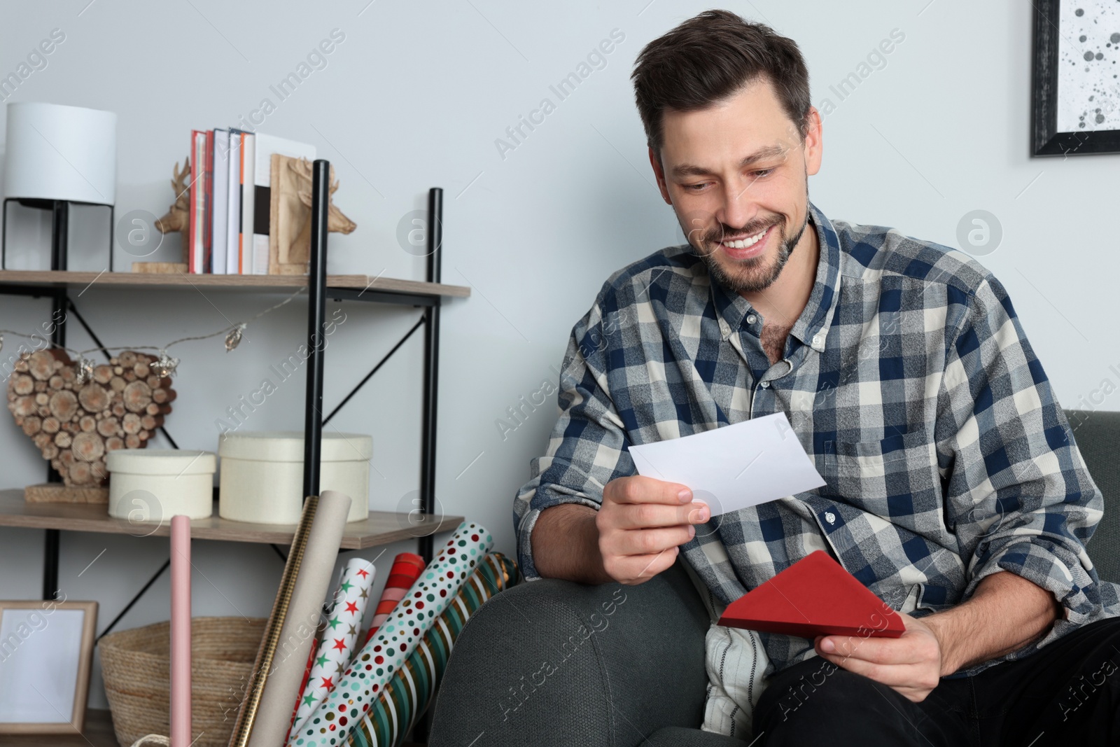 Photo of Happy man reading greeting card on sofa in living room