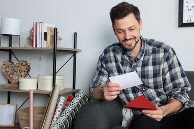 Happy man reading greeting card on sofa in living room