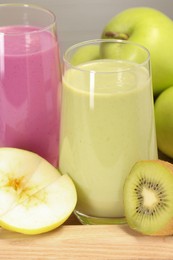 Glasses of different tasty smoothies and fresh ingredients on wooden tray, closeup