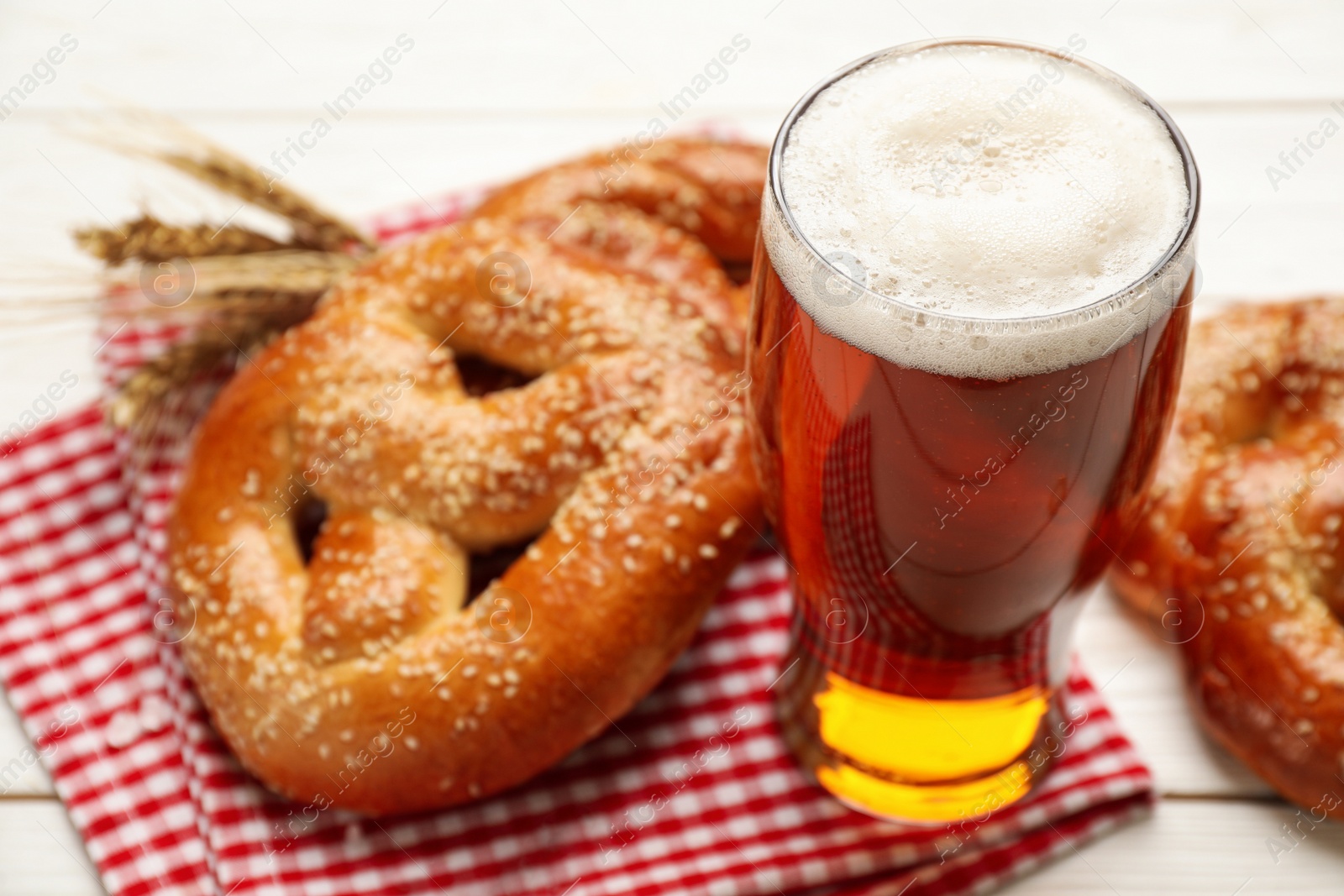 Photo of Glass of beer and tasty freshly baked pretzels on white wooden table, closeup