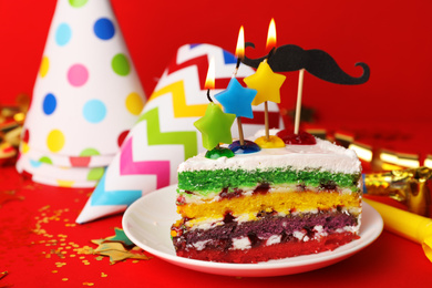 Piece of birthday cake with candles on red background