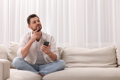 Photo of Man using smartphone on sofa near window with beautiful curtains in living room. Space for text