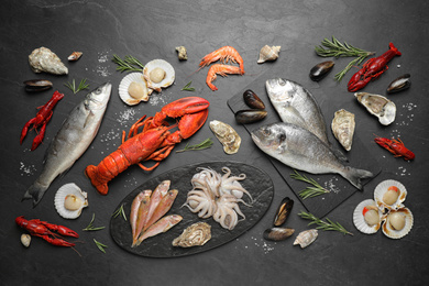 Fresh fish and different seafood on black table, flat lay